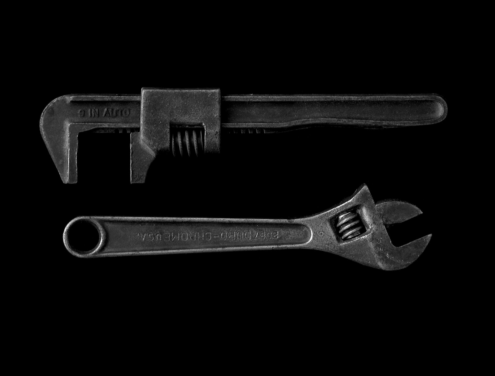 Two adjustable wrenches laid out on a dark bench before a job