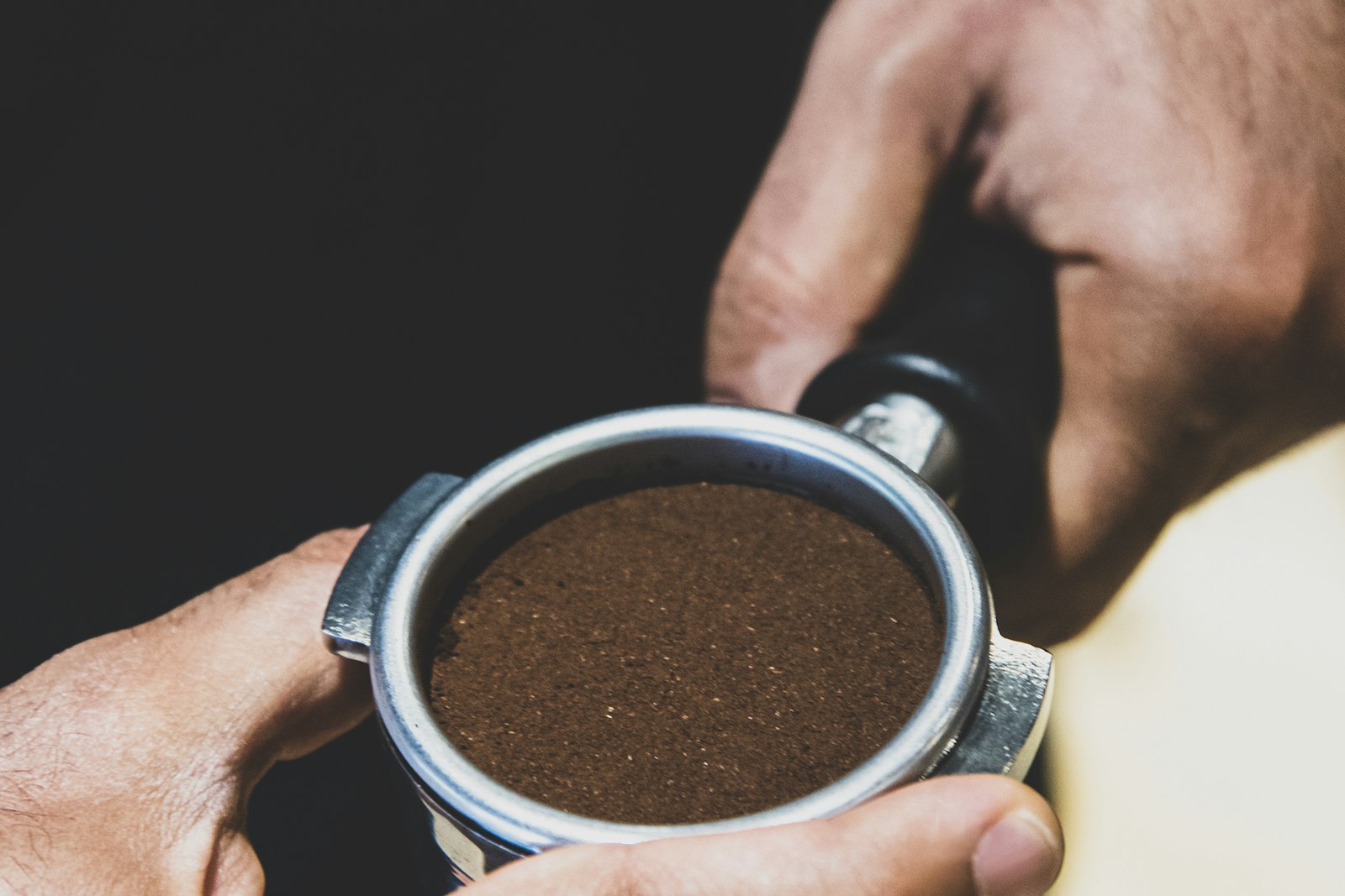 Hands holding a portafilter packed level with freshly ground coffee